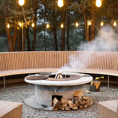 A large circula bench going around a fire pit in a forest, the bench is made from North American Douglas Fir slats