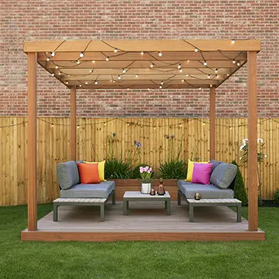 An outdoor pergola made with Timbersource's West African Sapele, with a table and chairs underneath, and fairy lights